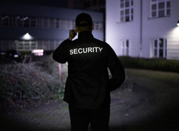 Security Guard Walking Building Perimeter With Flashlight At Night